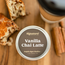 Load image into Gallery viewer, Vanilla Chai Latte soy candle in a 4 oz travel tin, from the Signature Collection by Angela Rose Studios, shown with a freshly-baked cinnamon swirl pastry, cinnamon sticks, and a cup of vanilla chai latte.